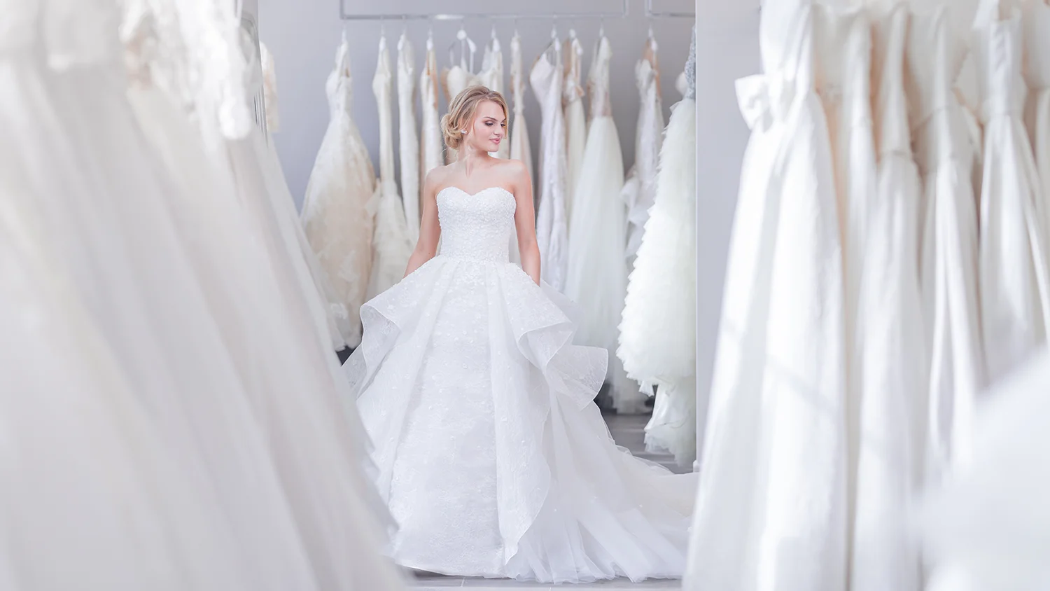 A bride tries on wedding dresses, surrounded by racks of dresses