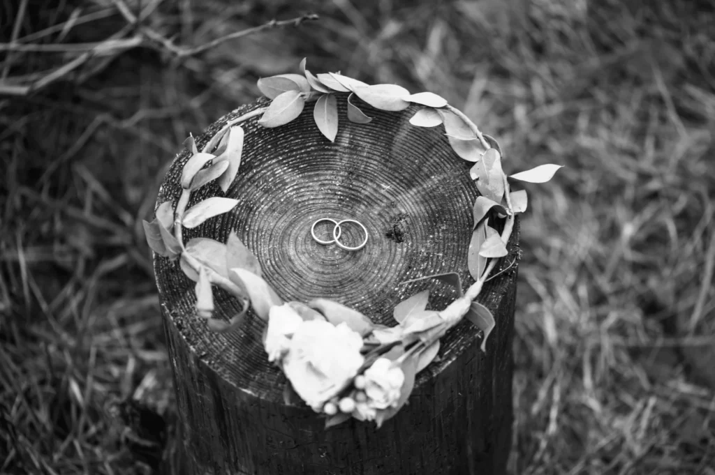 Wedding rings sit on a cut log with a floral wreath around them.