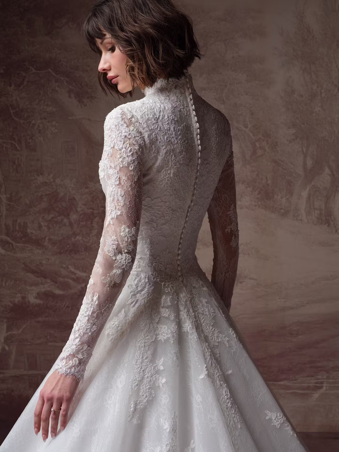 Dominique by Maggie Sottero modest lace A-line wedding dress with a high neckline, illusion long sleeves, basque waist, Chantilly lace, and hidden pockets.