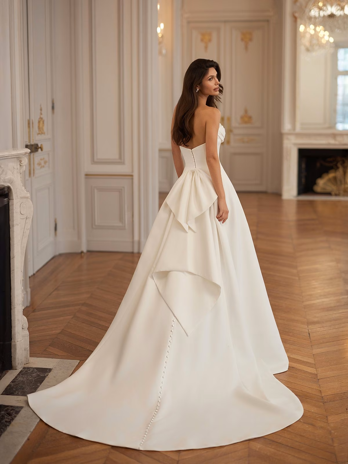 Annie by Moonlight Bridal crepe A-line wedding dress with a ruched sweetheart neckline, detachable bow, open back, and chapel train.