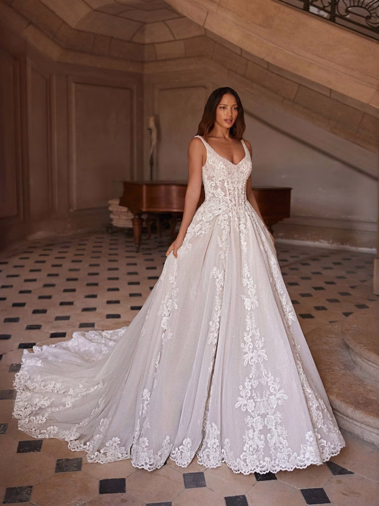 Monarque by Val Stefani sparkle A-line wedding dress with a basque waist, sweetheart neckline, illusion straps, embroidered lace, and chapel train.