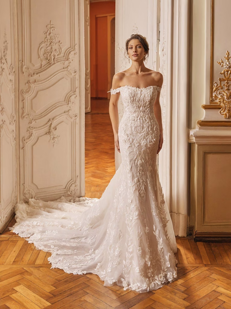 Regent by Val Stefani off-the-shoulder fit and flare wedding dress with 3D floral lace, sweetheart neckline, illusion side cutouts, V-back and cathedral train.